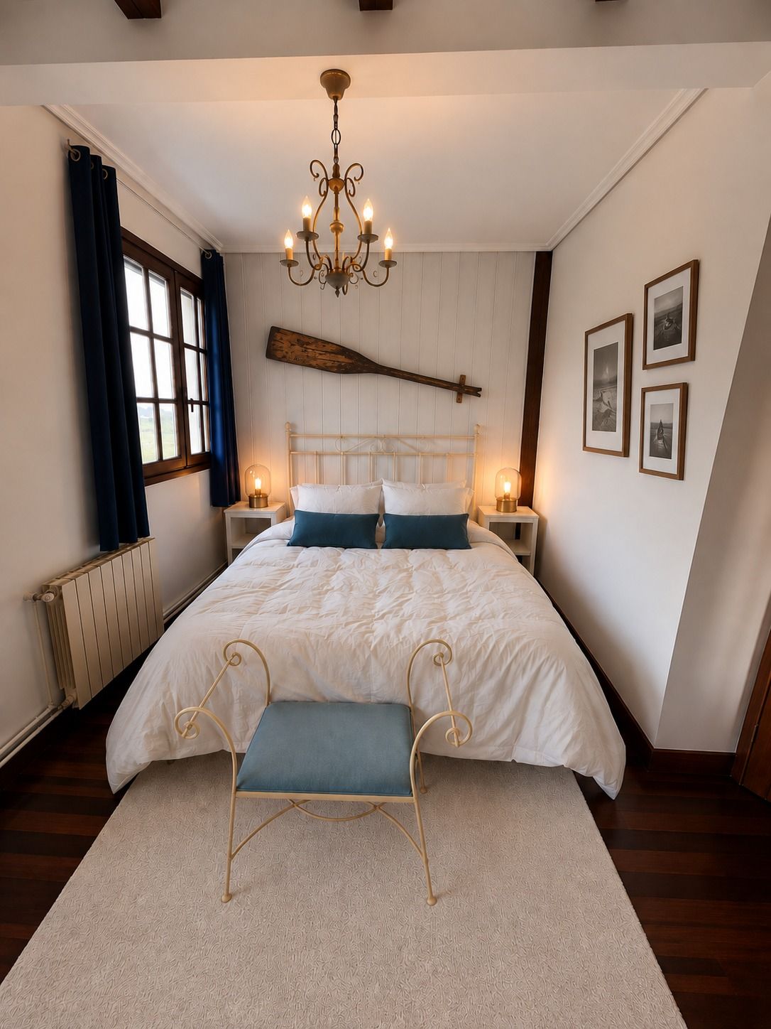 A bedroom with navy curtains, a ship's oar above the headboard and a gallery of framed boat photographs.