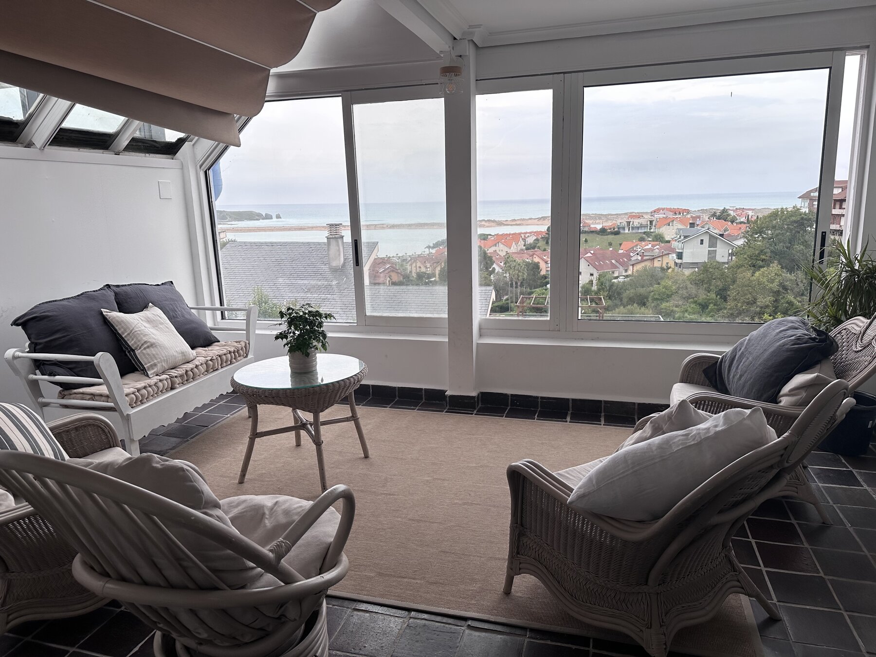 A sunroom with wicker chairs, looking out over the rooftops to the sea.