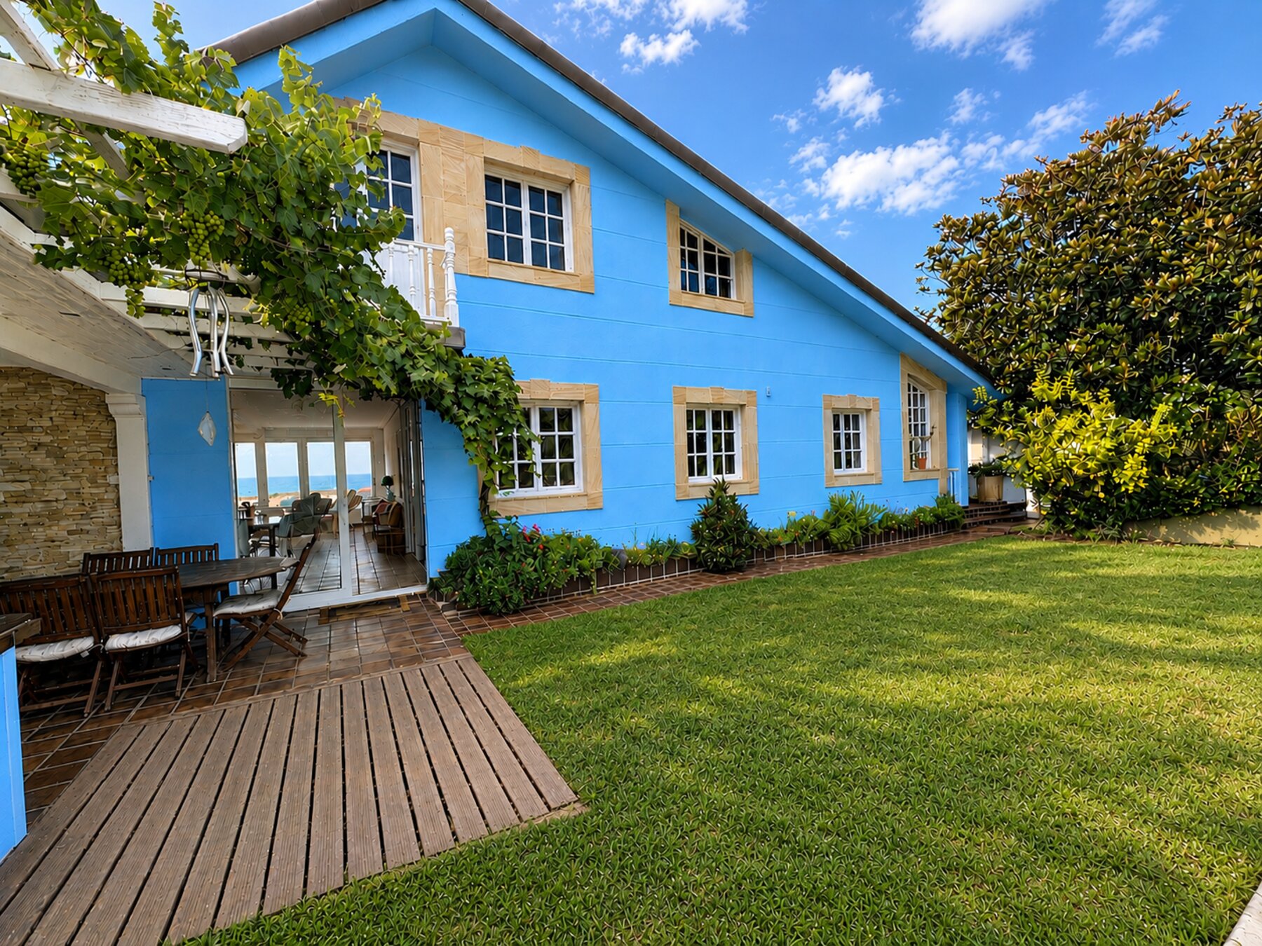The blue exterior of Casa Azul, framed by a grapevine-covered pergola and garden lawn.