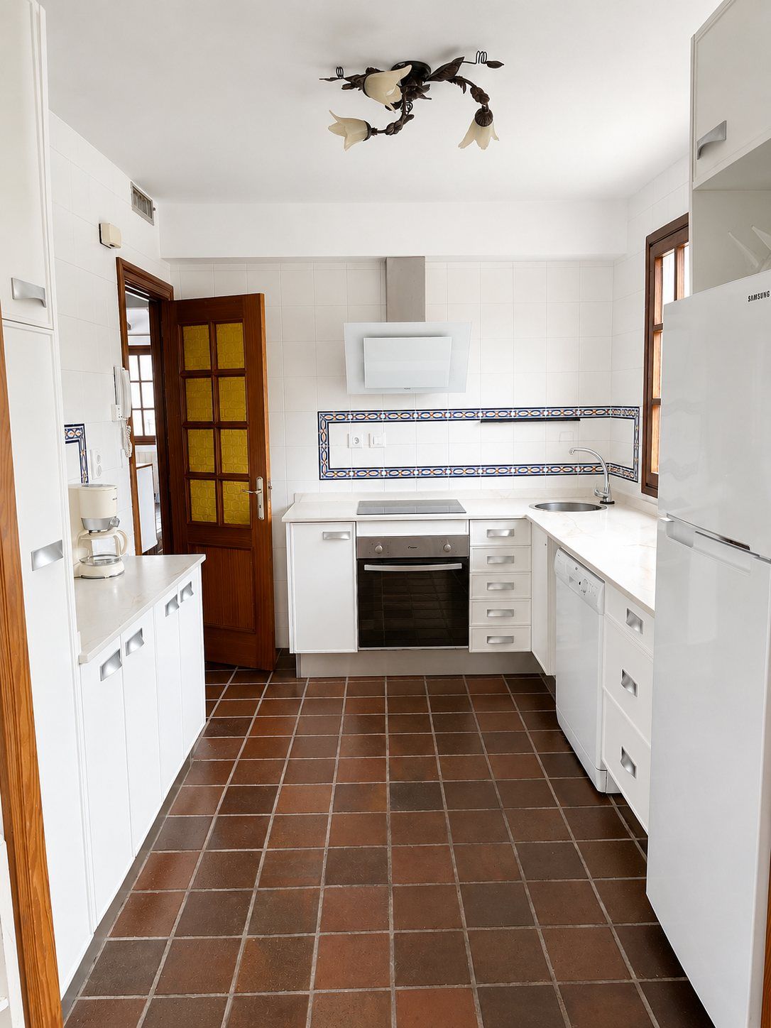 The white galley kitchen, with terracotta floor tiles.