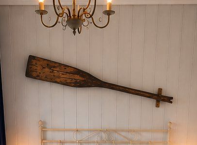 A wooden oar mounted on a wall above a bed.