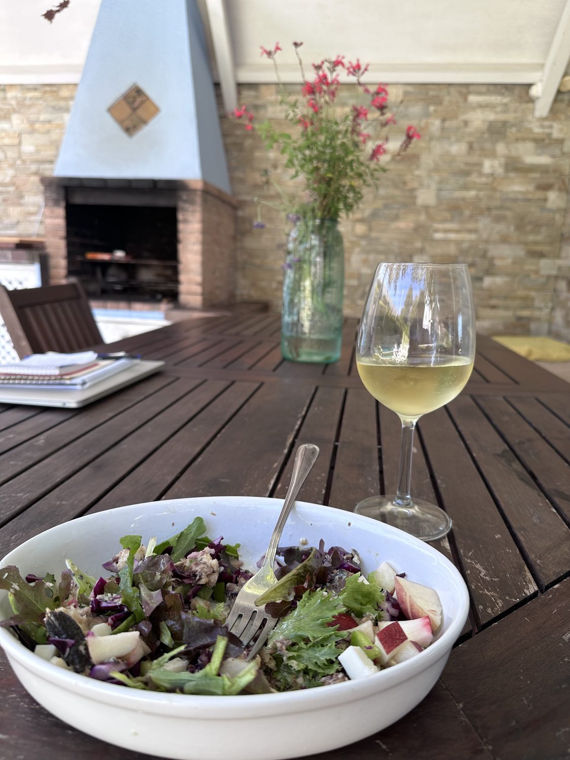 A salad and a glass of white wine on the patio table, in front of the barbecue.